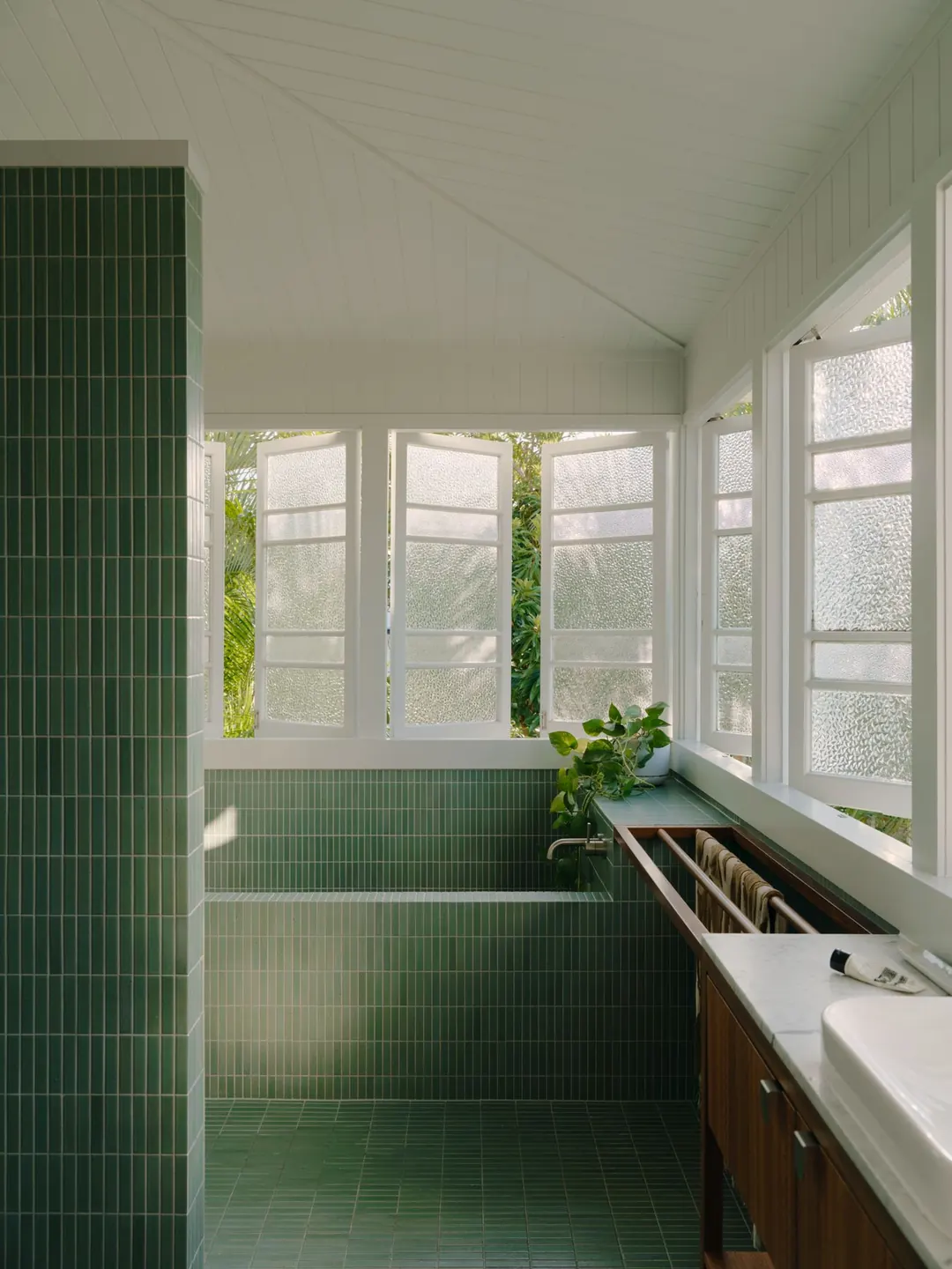 Upstairs bathroom in green finger tiles, with a tiled bath beneath a run of casement windows
