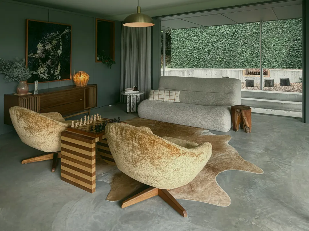 Swivel armchairs and a striped chess table in the garden room, the creeper wall beyond the glass