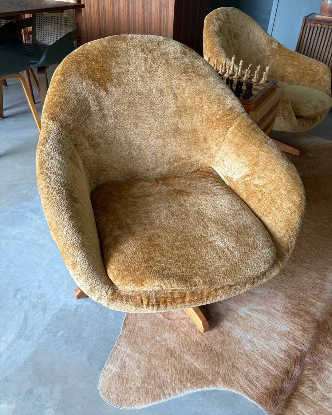 Mustard velvet swivel armchair with a timber star base on a cowhide rug, its twin beside the striped chess table